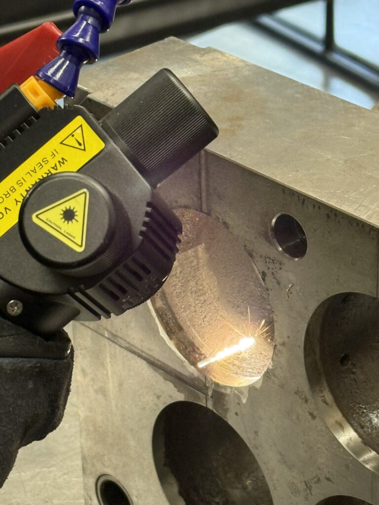 Cabezal de limpieza láser trabajando sobre una pieza metálica